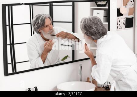 Reifer Mann, der sich im Badezimmer um seinen Bart und Schnurrbart kümmert Stockfoto