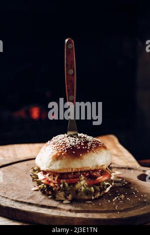 Saftiger Hamburger auf einem Holzständer auf schwarzem Hintergrund Stockfoto