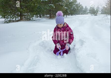 Ein kleines Mädchen sitzt im Schnee, macht Schneebälle Stockfoto