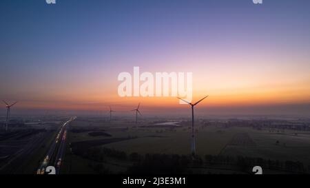 Luftaufnahme Sonnenaufgang von Wiesen und elektrischen Windmühlen über Hochgeschwindigkeitsautobahn am Morgen unter einem bunten Himmel natürliche Landschaft über der Panoramalandschaft. Hochwertige Fotos Stockfoto