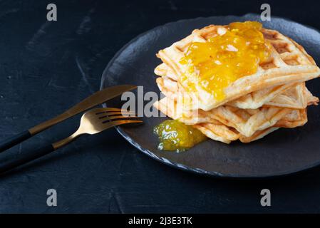 Hausgemachte leckere belgische Waffeln und Zitronenmarmelade auf dem schwarzen Tisch Stockfoto