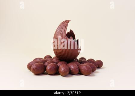 Ein großes zerbrochenes Schokoladenei, umgeben von kleinen Schokoladeneiern. Osterfeiertagskonzept Stockfoto