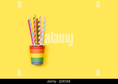Bunt gestreifte Trinkhalme in einem farbigen Einwegglas auf gelbem Hintergrund mit Platz zum Kopieren Stockfoto
