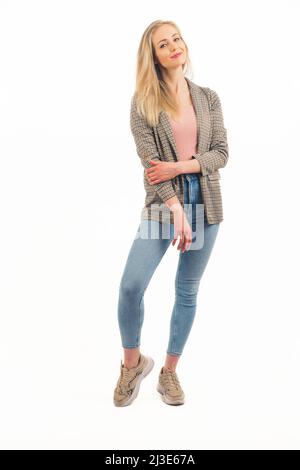 Attraktive europäische blonde Mädchen lächelnd stehend und berühren mit einer Hand zu zweiter trägt Jeans Snekaers und Jacke Studio shot voller Schuss weißen Hintergrund Kopie Raum. Hochwertige Fotos Stockfoto