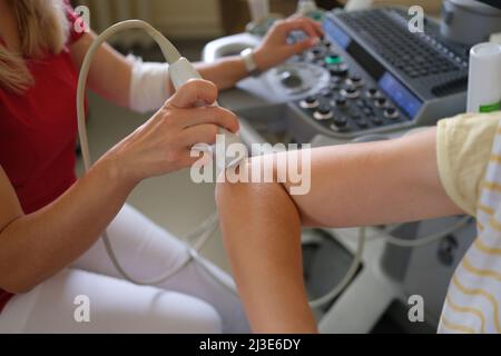 Der Arzt führt in der Klinik eine Ultraschalluntersuchung des Ellenbogens des Patienten durch Stockfoto