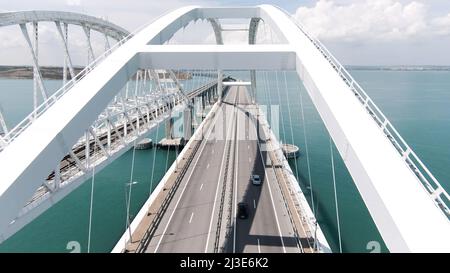 Schöne Landschaft aus einem Hubschrauber. Aktion. Der Blick von der Drohne auf die große weiße Brücke, auf der sich Autos über den Ozean bewegen. Stockfoto