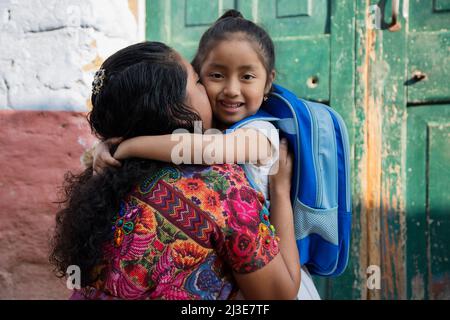 Die hispanische Maya-Mutter umarmte ihre kleine Tochter für ihren ersten Schultag – kleines Mädchen mit ihrer Mutter, die bereit ist, zur Schule zu gehen – Zurück zur Schule Stockfoto