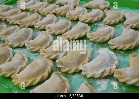 Ungekochte Knödel auf einem grünen Küchentablett mit Mehl zubereitet und bereit zum Kochen. Knödel oder Varenyks mit verschiedenen Füllungen sind traditionelle Ukr Stockfoto