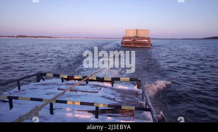 Containerschiff segelt auf einem breiten schönen Fluss auf Sonnenuntergang Himmel Hintergrund. Clip. Transportkonzept, Blick vom Frachtschiff. Stockfoto