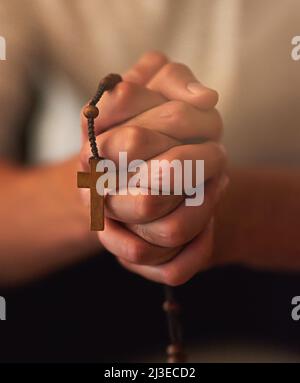 Das Gebet ist die beste Rüstung gegen alle Prüfungen. Ausgeschnittene Aufnahme eines Mannes, der einen Rosenkranz hält und betet. Stockfoto