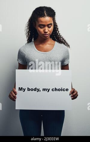 Mein Körper, mein Leben, meine Wahl. Studioaufnahme einer attraktiven jungen Frau, die ein Plakat mit meinem Körper, meiner Wahl vor einem grauen Hintergrund hält. Stockfoto