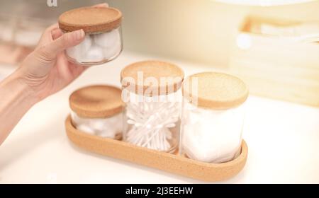 Weibliche Hand, die die Glasflasche mit dem Wattepad innen öffnet, um Make-up auf den Tisch im Schlafzimmer zu entfernen. Stockfoto