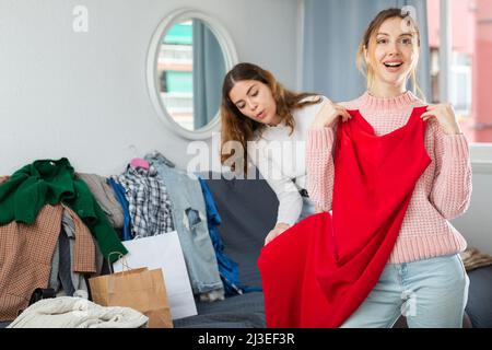 Freundinnen versuchen sich zu Hause ein neues rotes Kleid an Stockfoto