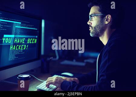 Er könnte für Sie kommen. Aufnahme eines fokussierten Computerhackers, der einen Computer im Dunkeln benutzt. Stockfoto