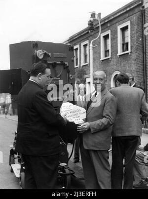 ALFRED HITCHCOCK posiert mit Box of Film am Drehort Candid on London Street mit VistaVision Camera with Movie Crew während der Dreharbeiten ZU DEM MANN, DER ZU VIEL WUSSTE 1956 Regisseur ALFRED HITCHCOCK Geschichte Charles Bennett und D.B. Wyndham-Lewis Drehbuch John Michael Hayes Kostümdesign Edith Head music Bernard Herrmann Filwite Productions / Paramount Pictures Stockfoto