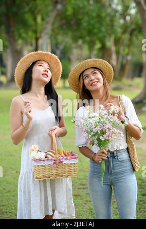 Zwei hübsche junge asiatische Freundinnen, die auf dem Gartenweg spazieren und gemeinsam eine wunderschöne Aussicht genießen. Stockfoto