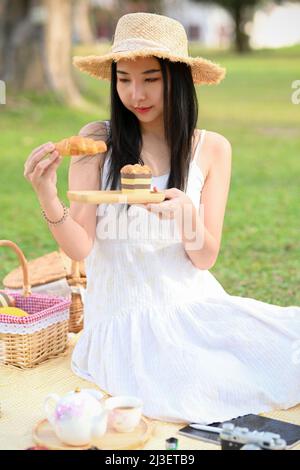 Portrait, hübsche junge asiatische Frau, die im Garten zu Mittag gegessen, Gebäck gegessen und an einem sonnigen Tag ein Picknick genossen hat. Stockfoto