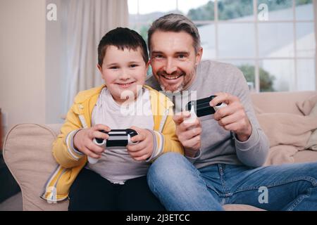 Nie ein schmerzlicher Verlierer. Aufnahme eines Vaters und eines Sohnes, der Videospiele spielt, während er sich zu Hause auf der Couch festklebt. Stockfoto