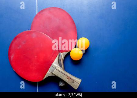 SURABAYA, INDONESIEN - 06. MÄRZ 2020: Zwei Tischtennis- oder Tischtennisschläger und -Kugeln auf einem blauen Tisch und Netz Stockfoto