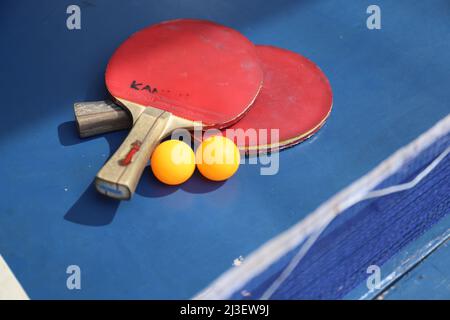 SURABAYA, INDONESIEN - 06. MÄRZ 2020: Zwei Tischtennis- oder Tischtennisschläger und -Kugeln auf einem blauen Tisch und Netz Stockfoto
