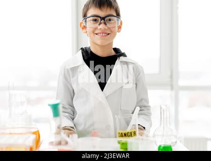 Schuljunge trägt Schutzbrille und macht Chemieexperiment in der Grundschule. Ein kluger Schüler, der die Kamera anschaut und im Labor lächelt Stockfoto