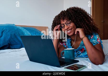 Junge afroamerikanische Frau im Bett, die zu Hause arbeitet Stockfoto