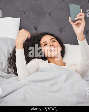 Der Morgen ist wunderbar. Aufnahme einer jungen Frau, die morgens im Bett lag und ihr Mobiltelefon benutzte. Stockfoto