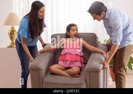 Eltern heben Sofa, während Tochter auf ihm sitzen Stockfoto