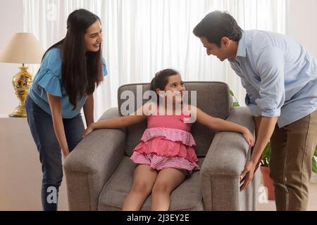 Eltern heben Sofa, während Tochter auf ihm sitzen Stockfoto
