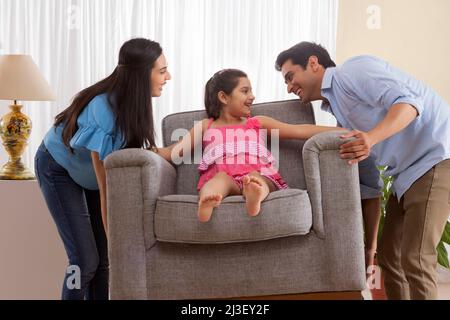Eltern heben Sofa, während Tochter auf ihm sitzen Stockfoto