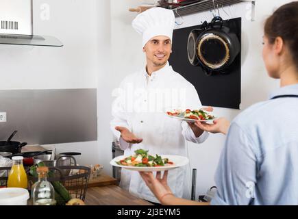 Lächelnde Kellnerin, die servierten Salat vom Koch nahm Stockfoto