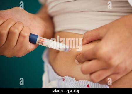 Der Körper weiß, wann Insulin benötigt wird. Nahaufnahme einer unkenntlichen Frau, die sich zu Hause mit Insulin in den Magen spritzt. Stockfoto