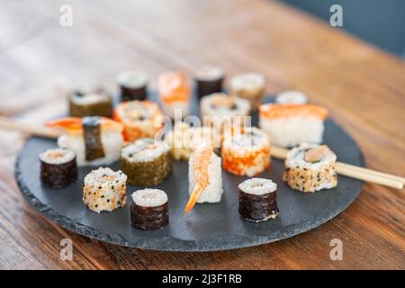 Steinplatte mit Sushi auf Holztisch Stockfoto
