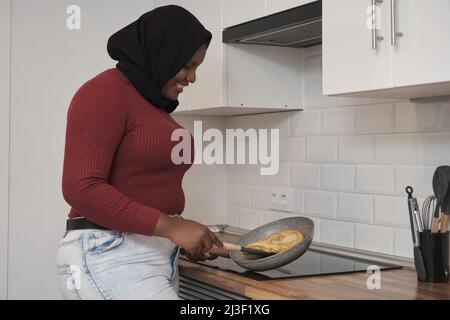 Junge muslimische Frau lächelt und bereitet spanisches Kartoffelomelett zu. Stockfoto