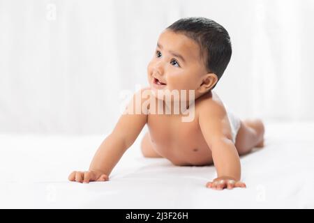 Niedliches Baby in Windel kriecht auf dem Bett