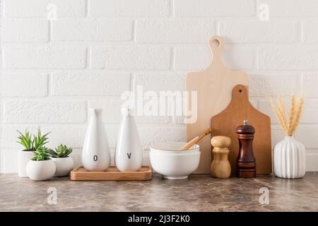 Verschiedene Küchenutensilien auf einer Marmorplatte in einer modernen Küche. Das Konzept der Einrichtung vor dem Hintergrund einer weißen Ziegelwand Stockfoto
