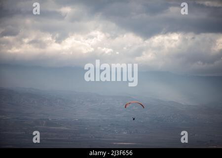 Bild eines Gleitschirms, der alleine fliegt, gegen einen grau bewölkten Himmel. Stockfoto