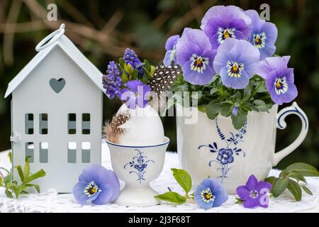 osterdekoration mit Strauß lila Blüten in Ei und Viola Blume in Tasse Stockfoto