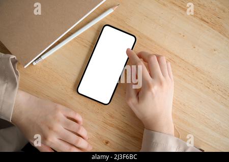 Eine Geschäftsfrau oder eine Frau, die ein Smartphone verwendet, um mit ihren Freunden zu kommunizieren. Smartphone-Modell mit weißem Bildschirm auf Holztisch. Stockfoto