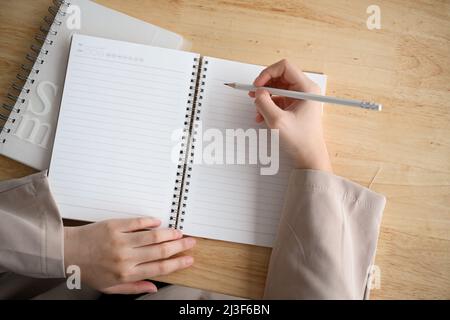 Overhead-Aufnahme, Frau, die einen Essay schreibt, Notizen macht, Hausaufgaben macht, wichtige Dinge auf einem leeren Spiralnotizbuch aufführt. Stockfoto