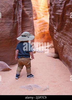 Kaukasischer Kleinkindjunge mit einem Safarihut, der im Wirepass Canyon in der Nähe von Buckskin Gulch, Coyote Buttes, steht. Stockfoto