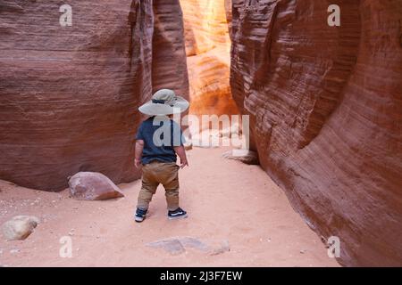 Kaukasischer Kleinkindjunge mit einem Safarihut, der im Wirepass Canyon in der Nähe von Buckskin Gulch, Coyote Buttes, steht. Stockfoto