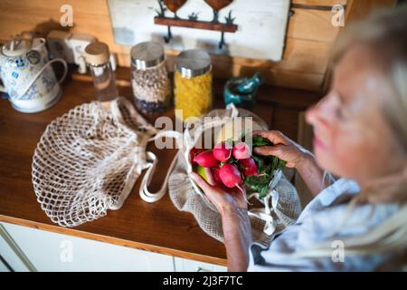 Nahaufnahme einer nicht erkennbaren älteren Frau, die zu Hause beim Auspacken von Einkaufen in Innenräumen einkauft, nachhaltiger Lebensstil. Stockfoto