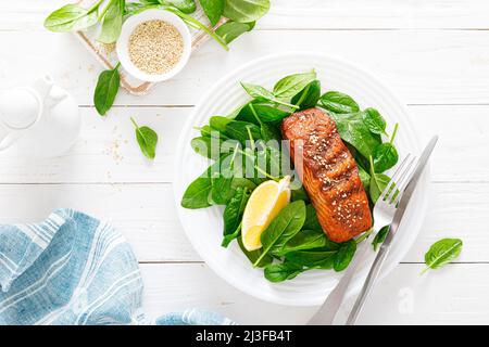 Lachsfischfilet vom Grill und frischer Spinatsalat auf dem Teller zum Mittagessen. Draufsicht Stockfoto