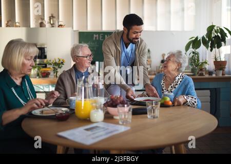 Eine Gruppe von fröhlichen Senioren, die im Pflegeheim frühstücken. Stockfoto