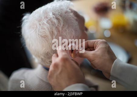 Nahaufnahme der Hand des Pflegepersonals, die ein Hörgerät in das Männerohr des Senioren einführt. Stockfoto