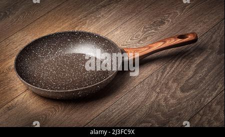 Moderne Bratpfanne mit Antihaftbeschichtung aus Granit, isoliert auf einem Hintergrund aus Holz. Stockfoto