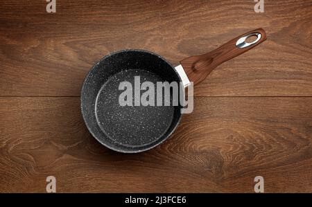 Moderne Bratpfanne mit Antihaftbeschichtung aus Granit, isoliert auf einem Hintergrund aus Holz. Stockfoto