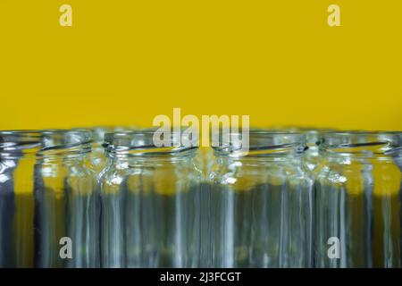 Frontale Aufnahme leerer Glasgefäße in einer Reihe auf einem gelb gefärbten Hintergrund. Ausgewählte Fokus oben auf dem Glas vor. Stockfoto