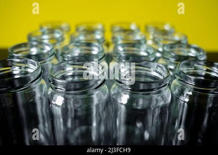 Frontale Aufnahme leerer Glasgefäße in einer Reihe auf einem gelb gefärbten Hintergrund. Ausgewählte Fokus oben auf dem Glas vor. Stockfoto